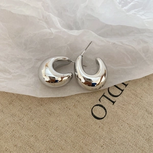 Close-up of polished silver C-shaped chunky hoop earrings with a mirror finish