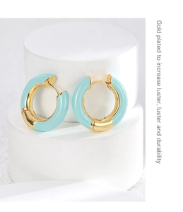 Detailed macro view of gold-plated teal enamel earrings on white display stand