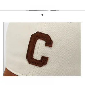 Detail of embroidered brown C letter patch on cream white cotton baseball cap