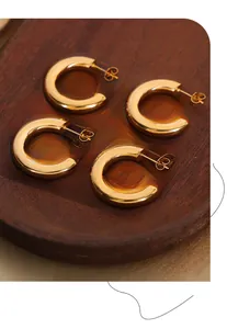 Detail view of two pairs of chunky gold-plated C-shaped hoop earrings on wooden tray