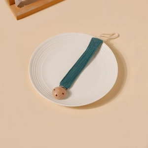 Détail de l'attache-tétine avec sangle en coton vert foncé et clip en bois de hêtre naturel