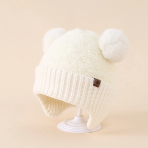 Dettaglio del cappello in maglia beige per neonati con due pompon e paraorecchie a coste