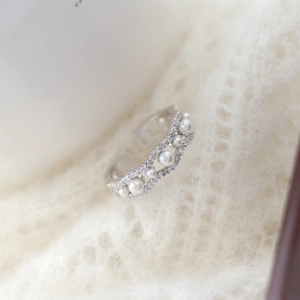 Detailed view of wave-shaped pearl ring with pavé zircons on soft white knit background