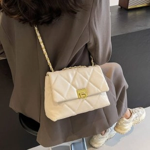 Quilted cream crossbody bag with gold chain strap worn over a dark blazer