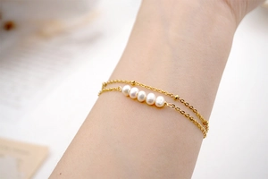Close-up of a double-layer golden steel bracelet with freshwater pearls on a woman's wrist