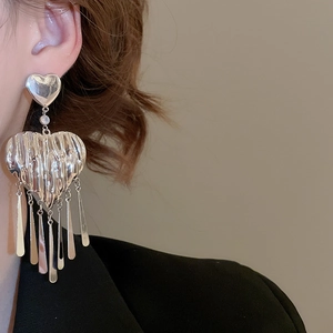 Detail of silver heart-shaped tassel earrings with ruffled texture worn on model