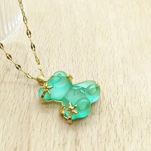 Close-up of translucent mint green resin bear pendant with gold stars on water wave chain