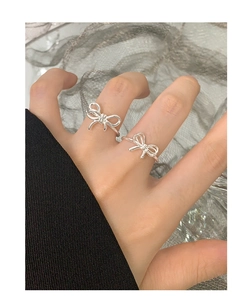 Detail shot of two irregular silver bow rings worn on fingers with a mesh background