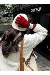 Detail of red wool knit gloves with white woven label worn by a model in winter outfit
