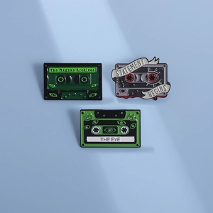 Trois pin's en émail en forme de cassettes d'horreur vertes sur un fond bleu clair
