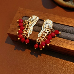 Dettagli di orecchini vintage dorati con perline rosse su espositore in legno scuro