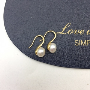 Macro shot of elegant white freshwater pearls hanging on delicate golden metal ear hooks
