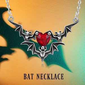 Gothic silver bat necklace with faceted red heart gemstone pendant on orange background