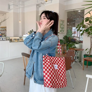 Detail shot of a red and white checkered corduroy tote bag carried by a model in denim