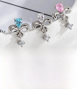 Detailed macro view of silver fleur-de-lis piercings with zircon stones in various colors