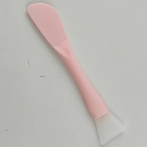 Close-up of a pink dual-ended silicone face mask brush with applicator and scraper