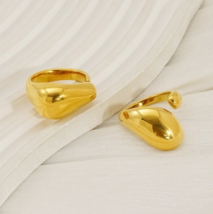 Close-up of golden teardrop fluid rings on a white textured tray for women