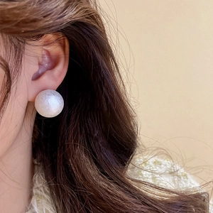 Close-up of a textured white cotton pearl stud earring on model with elegant finish