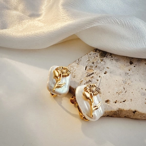Detail of gold flower design on baroque pearl earrings resting on elegant silk cloth