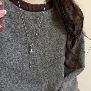 Detail of silver star pendant necklace worn over a charcoal grey knit sweater