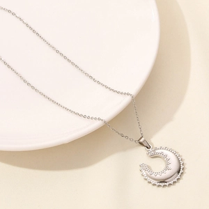 Detailed close-up of a silver crescent moon pendant with beaded texture on a white plate