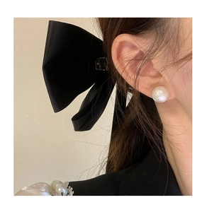 Detail view of white textured pearl earring and large black satin bow hair clip