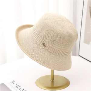 Elegant beige knitted bucket hat for women on a minimalist gold stand with fine texture