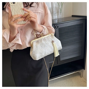 Close-up of white lace shell bag with rose patterns, gold clasp, and elegant fringe tassel