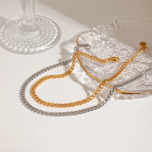 Detailed view of two-tone gold and silver Cuban chain anklets on a glass plate