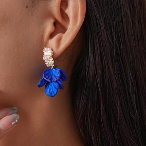 Gros plan d'un mannequin portant des boucles d'oreilles fleurs bleu cobalt et strass dorés