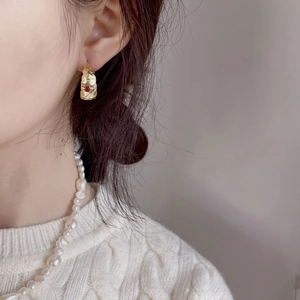 Detail of hammered gold earrings with red gemstone and minimalist pearl necklace style