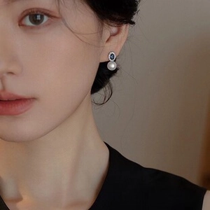 Close-up of elegant blue gemstone and baroque pearl earrings worn on a model's ear