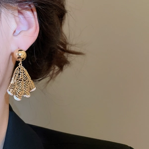 Macro view of a gold fan-shaped hollow drop earring worn by a model in black