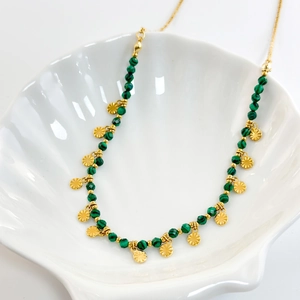 Detail of natural malachite beads and gold relief pendant on a white shell plate