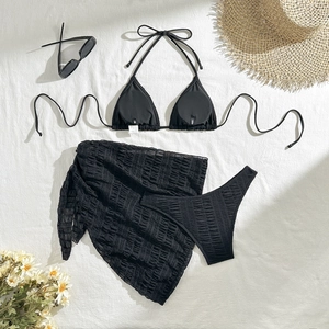 Flat lay of black three-piece bikini set with sheer mesh sarong and holiday accessories