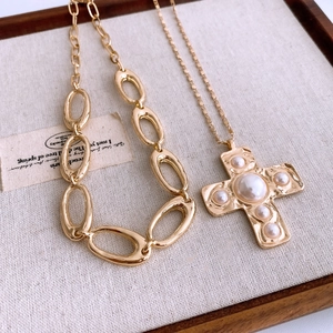 Macro detail of golden cross pendant with pearls on a textured chunky link chain