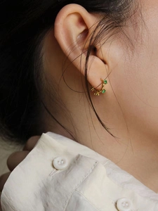 Détail d'une boucle d'oreille vintage en or sertie de zircons verts sur une mannequin