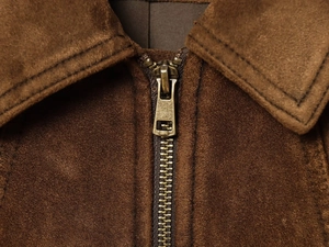 Gros plan d'une veste en daim marron montrant le zip en bronze et le détail du tissu