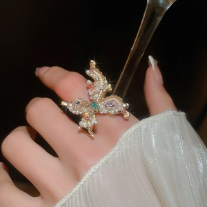 Detail view of a luxury gold butterfly ring with pink gemstones and pearls on hand
