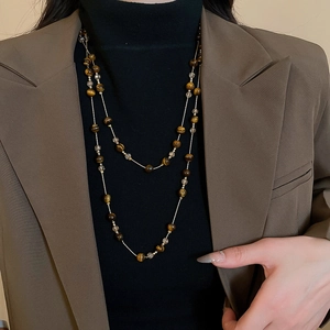 Detail of layered brown tiger eye stone beaded necklace on a model wearing a brown blazer