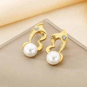 Detail of gold heart earrings with pearl drop and rhinestone on beige texture background