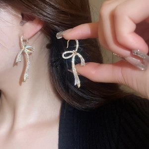 Close-up of gold-plated bow earrings with shimmering zircons on a model