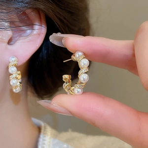 Detail of C-shaped gold-plated hoop earrings featuring white pearls and zircon accents