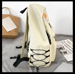 Side view of cream canvas backpack featuring side pockets and decorative round badges