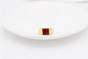 Macro detail of a gold signet ring featuring a square-cut red gemstone in a wide band