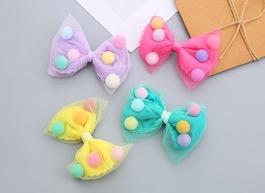 Close-up of mesh bow hair clips with colorful pom poms in purple and pink tones