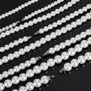 Detail view of multi-size round white pearl necklaces with silver clasps on black surface