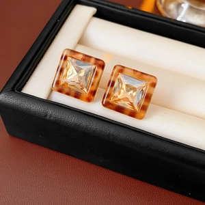 Detail of square tortoiseshell resin earrings with amber crystal in a black jewelry box