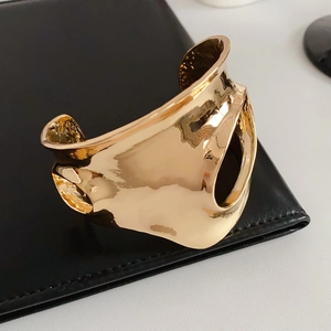 Détail d'un bracelet manchette doré ondulé et ajouré posé sur une surface en cuir noir