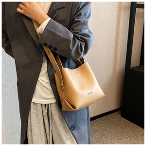 Brown leather bucket bag with gold logo on a model in a gray coat street style